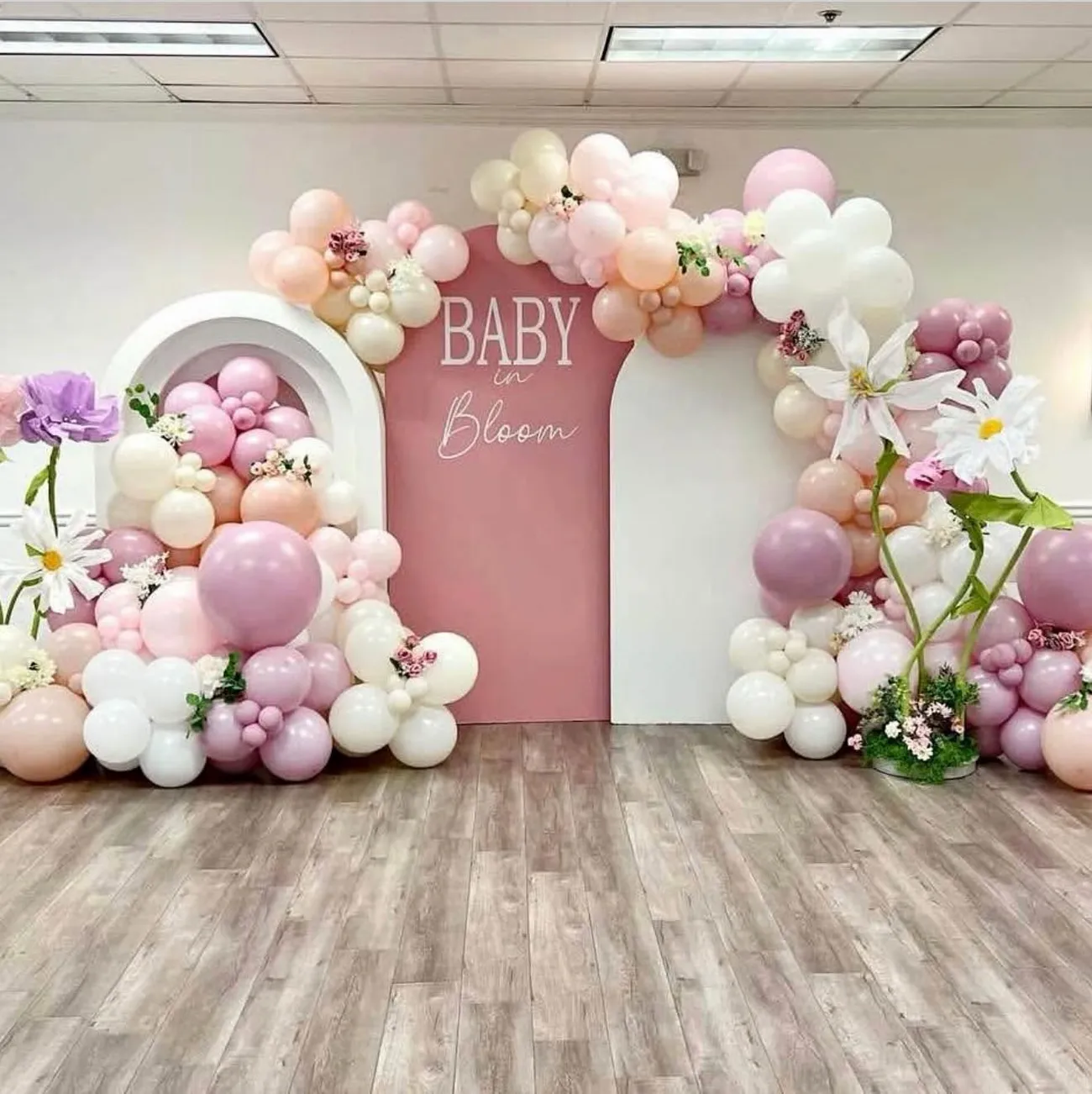 Baby in Bloom baby shower: arched backdrops wrapped in blush, mauve, and cream balloon garlands with oversized florals
